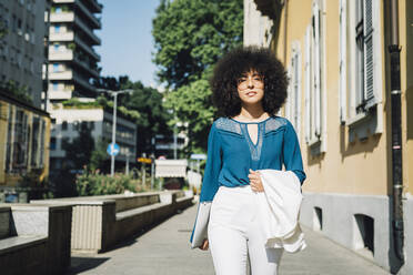 Young Afro businesswoman with laptop walking in city on sunny day - MEUF06870