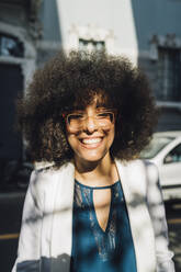 Glückliche Geschäftsfrau mit Afrofrisur und Brille an einem sonnigen Tag - MEUF06881