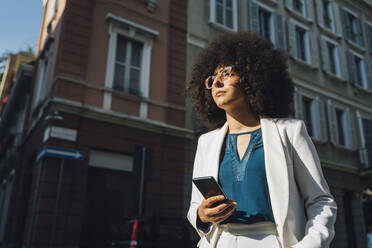 Junge Geschäftsfrau mit Mobiltelefon an einem sonnigen Tag - MEUF06884