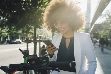 Happy businesswoman with push scooter using phone in city - MEUF06890