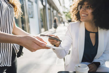 Young businesswoman paying through smart phone at sidewalk cafe - MEUF06894