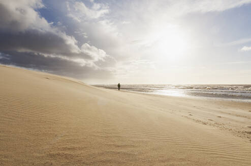 Wolken über Sandstrand bei Sonnenuntergang mit Silhouette von Mann zu Fuß im Hintergrund - GWF07507