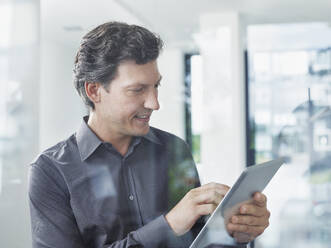 Smiling businessman using tablet PC in office - RORF02899