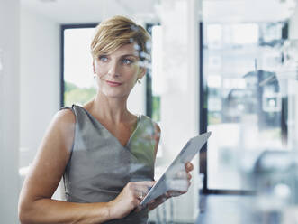 Nachdenkliche Geschäftsfrau mit Tablet-PC im Büro stehend - RORF02901