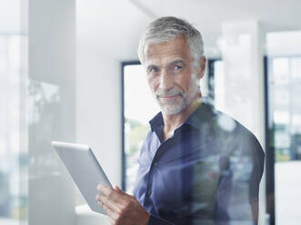 Smiling mature businessman with tablet PC seen through glass - RORF02908