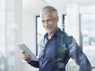 Smiling businessman with tablet PC standing in office - RORF02910