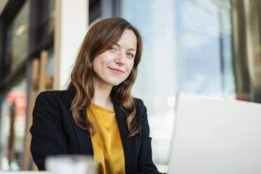 Smiling businesswoman with brown hair using laptop at cafe - DIGF18231