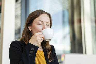 Geschäftsfrau mit geschlossenen Augen genießt Kaffee in einem Cafe - DIGF18238