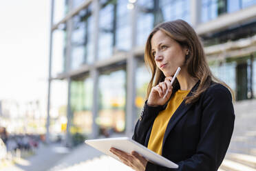 Thoughtful businesswoman with hand on chin holding tablet PC and digitized pen - DIGF18246