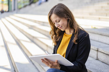 Lächelnde Geschäftsfrau mit Tablet-PC auf einer Treppe sitzend - DIGF18248