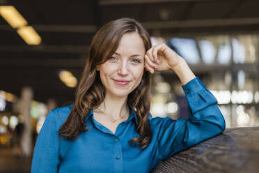 Smiling woman wearing blue shirt leaning on wall - DIGF18289