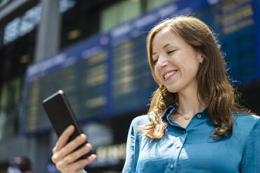 Lächelnde Frau mit Smartphone an einem sonnigen Tag - DIGF18291