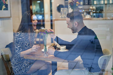 Durch Fenster Seitenansicht von lächelnden Freund Fütterung optimistisch Freundin beim Sitzen am Tisch in modernen Licht Cafeteria während Datum - ADSF35740