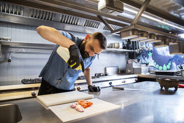 Männlicher Koch gießt Speiseöl auf geschnittene Zwiebeln und Tomaten in einer Restaurantküche - ADSF35755