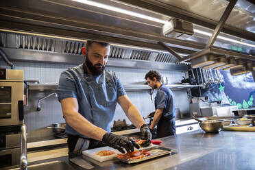 Chef wearing gloves cleaning shrimp at kitchen counter in restaurant - ADSF35757