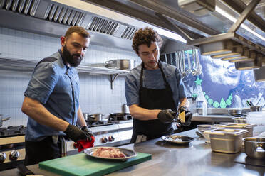 Caucasian chefs preparing dish for customer in commercial kitchen - ADSF35758