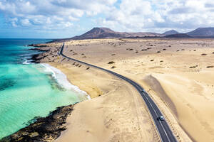 Luftaufnahme einer Straße durch die Wüste mit Blick auf das kristallklare Meer, Naturpark Corralejo, Fuerteventura, Kanarische Inseln, Spanien, Atlantik, Europa - RHPLF22449
