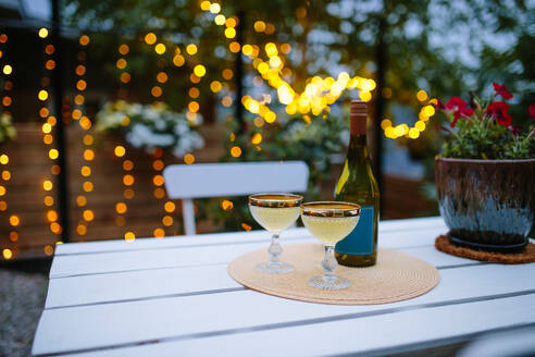 Gläser mit Champagner serviert auf weißen Holztisch mit Flasche auf der Terrasse des Gebäudes mit Bäumen gegen unscharfen Hintergrund - ADSF35797