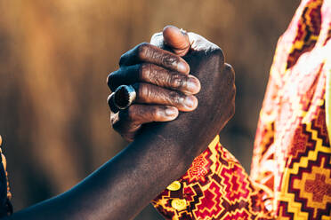 Unerkennbare schwarze Menschen in traditioneller afrikanischer Kleidung, die sich an einem sonnigen Tag die Hände schütteln - ADSF35845