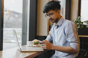 Freelancer using smart phone at table in cafe - OSF00324