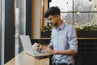 Junger Freiberufler arbeitet am Laptop in einem Café - OSF00326