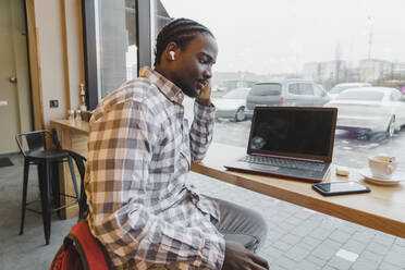 Young student wearing wireless in-ear headphones sitting at table - OSF00334