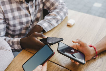 Gemischtrassige Freunde mit Smartphones am Tisch im Café - OSF00350