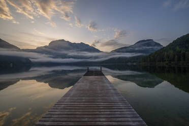 Austria, Styria, Altaussee, Jetty on shore of lake Altaussee at foggy dawn - RUEF03753