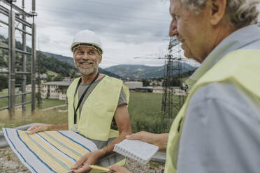 Lächelnder Ingenieur, der einen Plan hält und einen Mitarbeiter ansieht - MFF09267