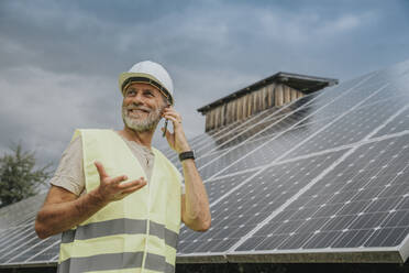 Engineer wearing hardhat talking on phone by solar panels - MFF09274