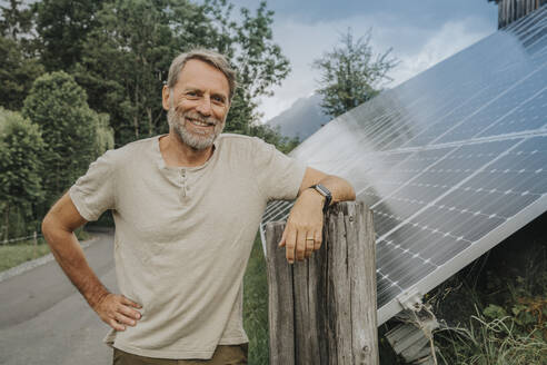 Smiling mature man standing on road by solar panel - MFF09277