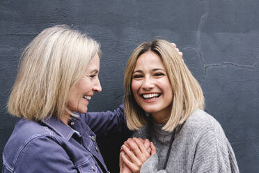 Glückliche blonde Mutter und Tochter halten Hände vor der Wand - ASGF02528
