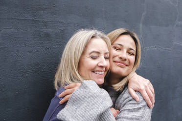 Lächelnde Mutter und Tochter mit geschlossenen Augen, die sich gegenseitig umarmen - ASGF02529