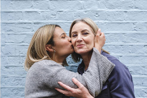 Junge Frau küsst ihre Mutter vor einer blauen Wand - ASGF02539