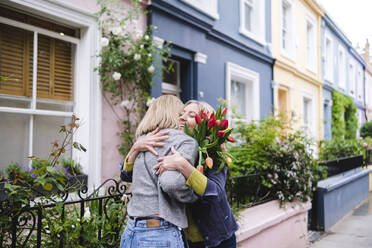 Mutter und Tochter mit Tulpenblüten umarmen sich in der Stadt - ASGF02557