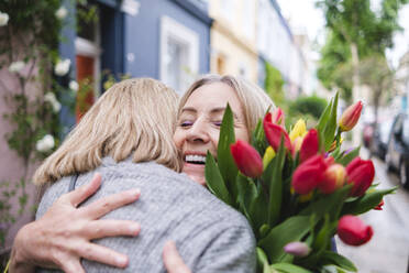 Happy senior woman with flowers embracing daughter - ASGF02558