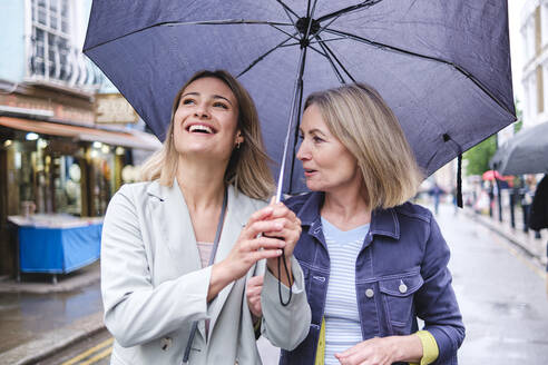 Mother and daughter with umbrella walking together on street - ASGF02560
