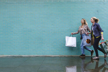 Glückliche Mutter und Tochter mit Einkaufstüten, die zusammen auf dem Fußweg laufen - ASGF02579