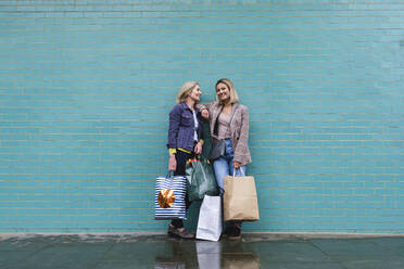 Lächelnde Tochter und Mutter mit Einkaufstüten vor einer blauen Wand - ASGF02580