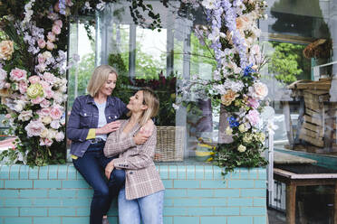 Smiling mother and daughter outside flower shop - ASGF02583