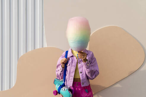 Woman covering face with cotton candy in front of wall - VPIF06691