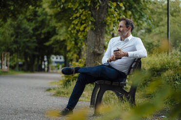 Älterer Geschäftsmann mit Mobiltelefon auf einer Bank im Park sitzend - JOSEF11128