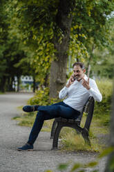 Geschäftsmann, der mit seinem Handy spricht, sitzt auf einer Bank im Park - JOSEF11129