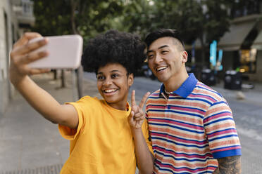 Glückliche junge Frau gestikuliert Friedenszeichen nehmen selfie auf Handy mit Mann - JCCMF06668