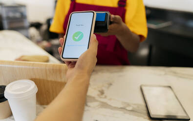 Hand of customer making contactless payment through smart phone in cafe - JCCMF06686