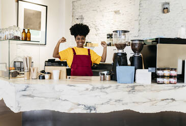 Smiling woman with Afro hairstyle flexing muscles at checkout - JCCMF06691