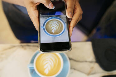 Hände einer jungen Frau, die eine Kaffeetasse mit ihrem Smartphone in einem Café fotografiert - JCCMF06704