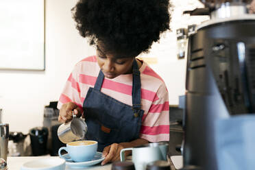 Woman with Afro hairstyle making coffee in cafe - JCCMF06705