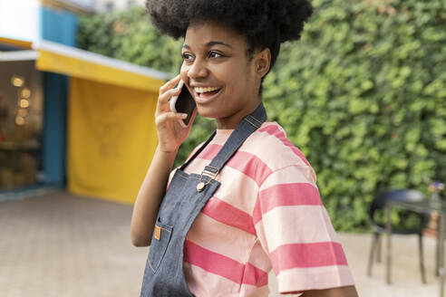 Glückliche Frau mit Afrofrisur im Gespräch mit einem Smartphone - JCCMF06718
