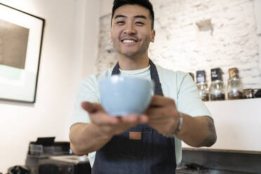 Glücklicher Mann bietet Kaffeetasse an - JCCMF06737